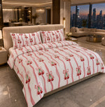 A made bed in a modern bedroom setting, featuring a white duvet cover and matching pillowcases printed with vertical pink stripes and clusters of red cherries with green stems.